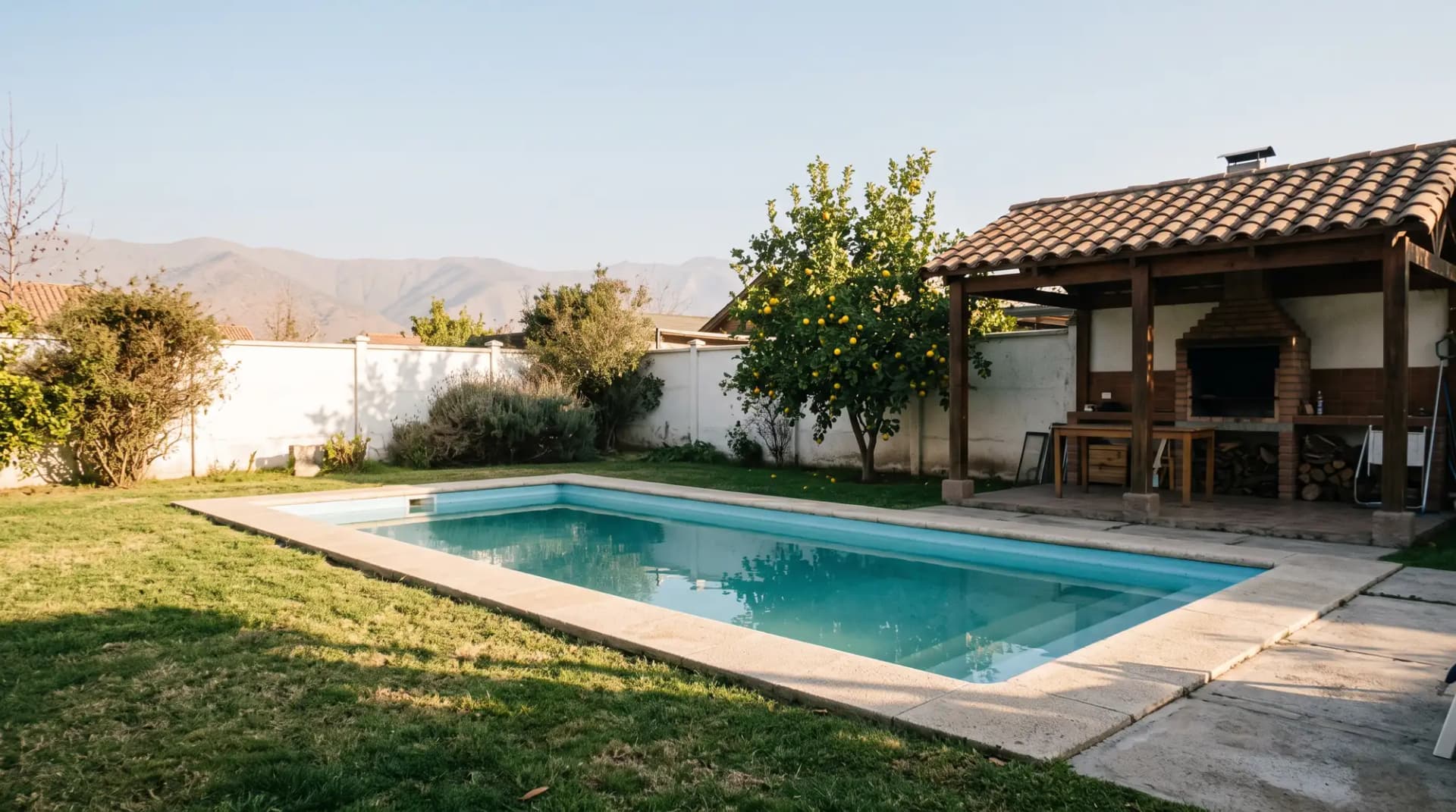 Patio de una casa al atardecer con una piscina de fibra de vidrio rectangular, quincho y un limonero